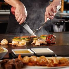 a chef is preparing food on a grill with tongs and chopsticks in his hand