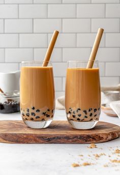 two glasses filled with liquid sitting on top of a cutting board next to each other