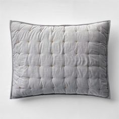 a white pillow with grey piping on the front and back, against a white wall