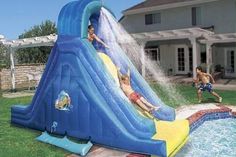 two children are sliding down an inflatable water slide that is on the lawn