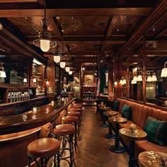 a restaurant with wooden tables and stools in front of the bar, lights on