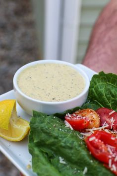 a white plate topped with lettuce and tomatoes next to a bowl of dip