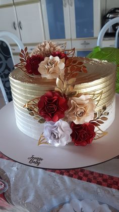 a three layer cake decorated with flowers and gold leaf decorations on top of a table