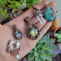 a person's hand holding five different rings and pendants in front of some succulent plants