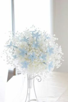 a vase filled with white and blue flowers sitting on top of a table next to a window