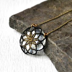 a black and gold necklace with a flower in the center on a stone slab next to a rock