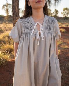 a woman standing in front of a tree wearing a dress with ruffles on it