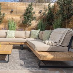 a couch and coffee table sitting in front of a wooden fence with plants on it