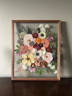 a wooden frame with flowers in it sitting on a table next to a white wall