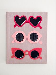 a pink and black wall hanging with sunglasses on it's face, heart shaped frames in the shape of glasses