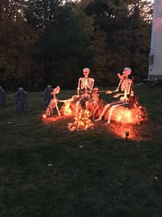 three skeletons sitting on top of a fire pit in the middle of a yard with halloween decorations around them