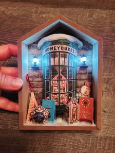 someone is holding up a miniature toy store in the shape of a house with lights on