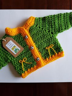 a green and yellow knitted sweater sitting on top of a white table next to a tag