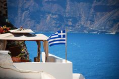 an umbrella and flag on the roof of a building overlooking water with mountains in the background