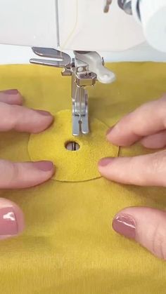 two hands are working on a sewing machine with yellow fabric and silver scissors in front of them