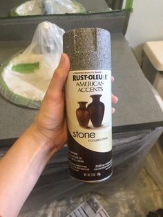 a person holding up a can of stone in front of a counter with other items on it