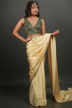 Embrace the beauty of the Cassandra Cream Satin Gold Trim One Minute Saree made with a gold sequin border. Styled with a art silk blouse in bottle green color. Perfect for your next festive occasion. Product Features: Saree Color: Cream Blouse Color: Bottle Green Saree Fabric: Satin Blend Blouse Fabric: Art Silk Blouse In Green Saree Work: Gold Sequin Border Saree Wash Care: Dry Clean Occasion: Party , Cocktail Party ,Wedding Reception Package Content: Saree Disclaimer: There will be slight diff Golden Saree With Green Blouse, Festive Gold Embellished Pre-draped Saree, Festive Embellished Chanderi Blouse Piece, Festive Silk Pre-draped Saree With Sequins, Gold Pre-draped Saree For Navratri Party, Sleeveless Silk Traditional Wear For Party, Gold Embellished Saree For Reception, Elegant Green Pre-draped Saree For Celebration, Festive Pista Green Pre-draped Saree For Party