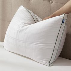 a person holding a pillow on top of a bed with white sheets and green piping