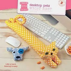 a cat stuffed animal next to a keyboard and mouse on a wooden table with the caption destop pets wrist rest