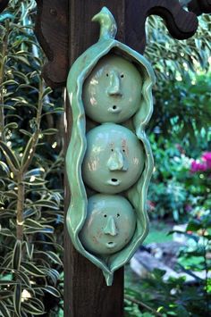 three peas in a pod with faces on them hanging from a wooden pole near some plants