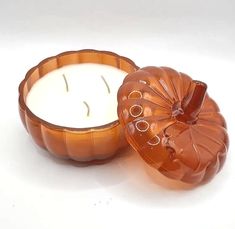 an orange pumpkin shaped candle sitting in front of a white background with the lid open