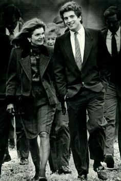 black and white photograph of two people walking next to each other with others in the background