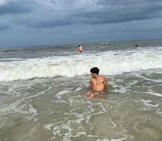 a man is sitting in the water at the beach while people are swimming in the ocean behind him