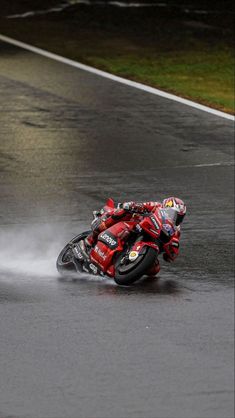 a man riding a motorcycle on top of a wet road next to a red car