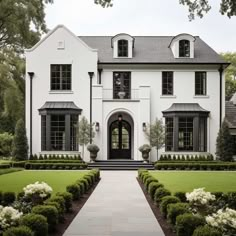 a large white house with lots of windows and bushes in front of the entrance to it