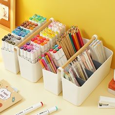 a white container filled with lots of different colored markers and pencils next to a yellow wall