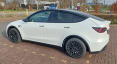 a white electric car parked in a parking lot next to a brick walkway and trees