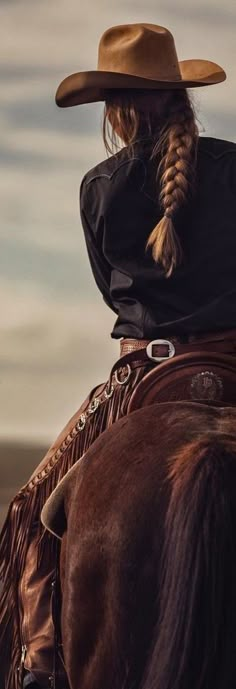 a woman wearing a cowboy hat riding on the back of a brown horse