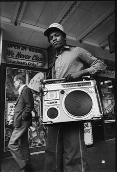 a man holding a boombox in front of a store sign with an advertisement on the wall behind him