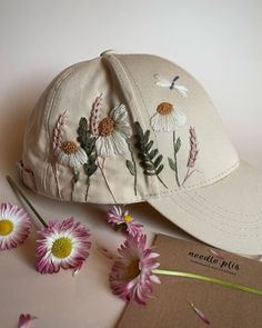 a baseball cap with flowers on it next to a notepad and some daisies