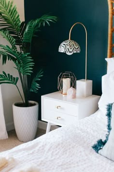 a bedroom with green walls, white bedding and two plants on the nightstands