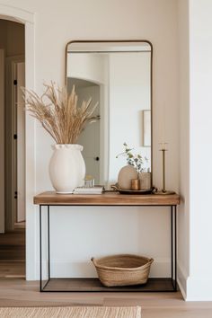 a white vase sitting on top of a wooden table next to a mirror and basket