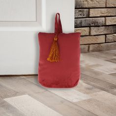 a red tote bag sitting next to a white door with a yellow tassel