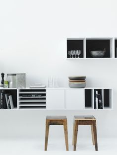 two wooden stools sitting next to each other in front of a white shelf filled with bottles and glasses