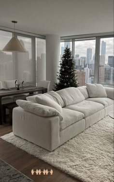 a living room filled with furniture and a christmas tree in front of two large windows