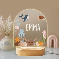 an illuminated personalized name sign with sea animals and marine creatures on it, next to a potted plant