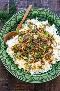 a green plate topped with rice and meat on top of a wooden table next to a spoon