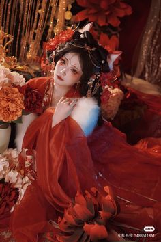 a woman dressed in red is sitting on the floor with flowers and candles around her