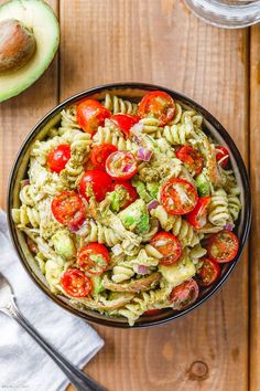 a bowl filled with pasta salad next to an avocado and fork on the side