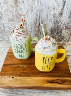 two mugs with whipped cream and sprinkles on them sitting on a wooden tray