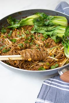 a wok filled with noodles and vegetables on top of a table