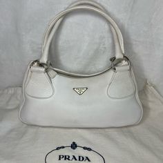 Prada Shoulder Bag By Miuccia Prada Vintage Sabbia Vitello Daino Leather Vitello Daino Leather & Enameled Metal Triangle Silver-Tone & Multitonal Hardware Rolled Handles Logo Jacquard Lining & Single Interior Pocket Zip Closure At Top Includes Authenticity Certificate **Prada Dust Bag Included** Estimated Item Measurements: Handle Drop: 8" Height: 7.25" Width: 13.5" Depth: 4.75" Color: White Please Look Closely At Each Pic And Angle To See Exact Condition & Dimensions. Flaws Noted: Loose Threads Where Handles Meet Bag; Minor Wear On Bottom Border Beading, A Couple Very Small Dark Spots (About The Size Of A Pen Point). Signs Of Wear/Use. Interior V Pre-owned Satchel Shoulder Bag, Elegant Pre-owned Travel Bags, Pre-owned Elegant Leather Shoulder Bag, Pre-owned Elegant Top Handle Bag, Pre-owned Elegant Shoulder Bag For Shopping, Elegant Pre-owned Leather Shoulder Bag, Elegant Pre-owned Top Handle Bag, Elegant Pre-owned Shoulder Bag For Shopping, Elegant Pre-owned Rectangular Bag