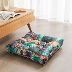 a multicolored patchwork floor cushion sits on the floor next to a coffee table