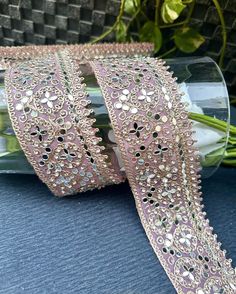 two rolls of pink ribbon with sequins and beads on them sitting next to some flowers