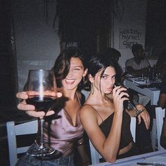 two women sitting at a table with wine glasses in front of them and one holding a cell phone to her ear