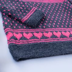 a knitted sweater with pink hearts on the front and black sleeves, sitting on a white surface